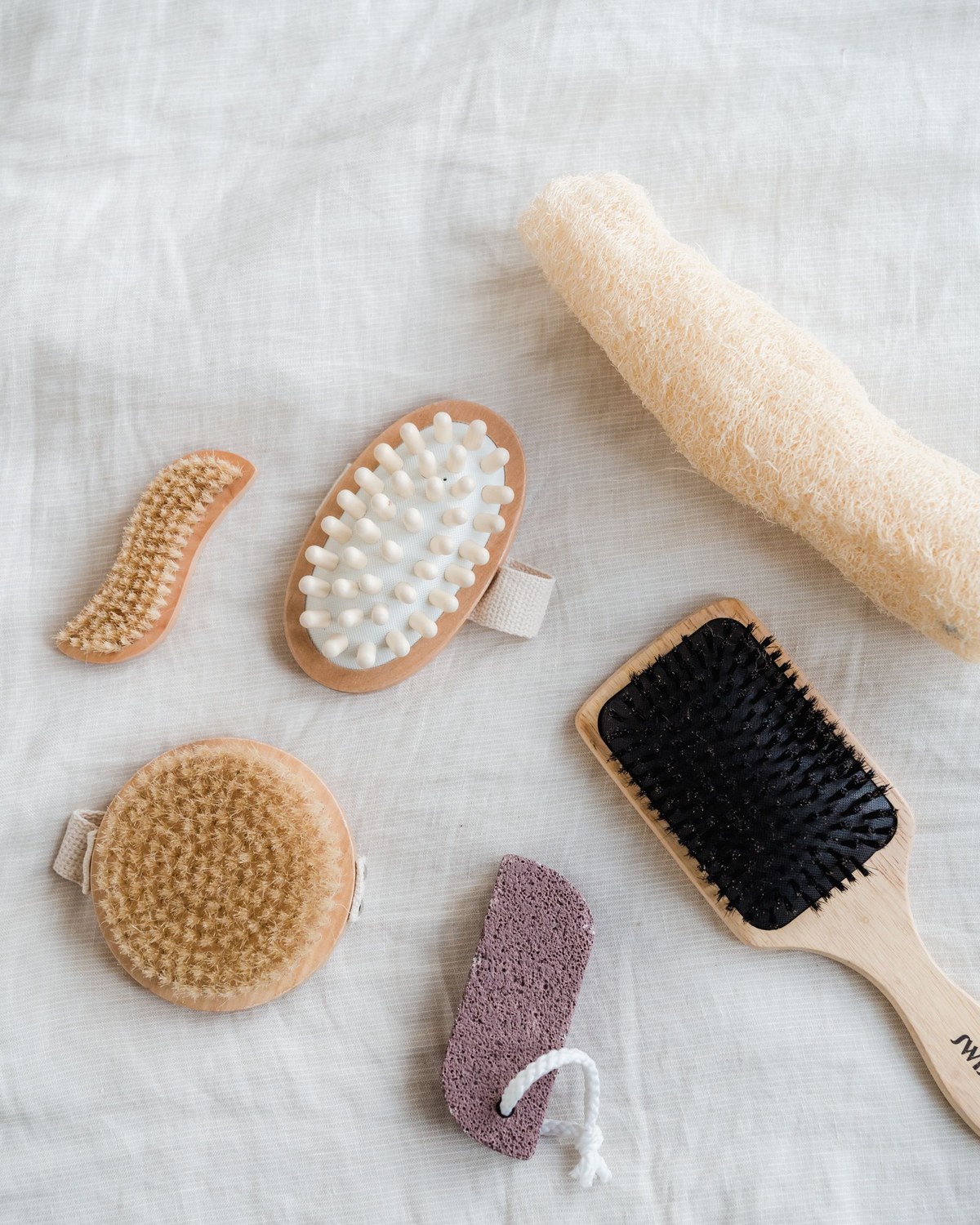 Natural body-care tools - wooden brushes, loofah and pumice - laid on linen