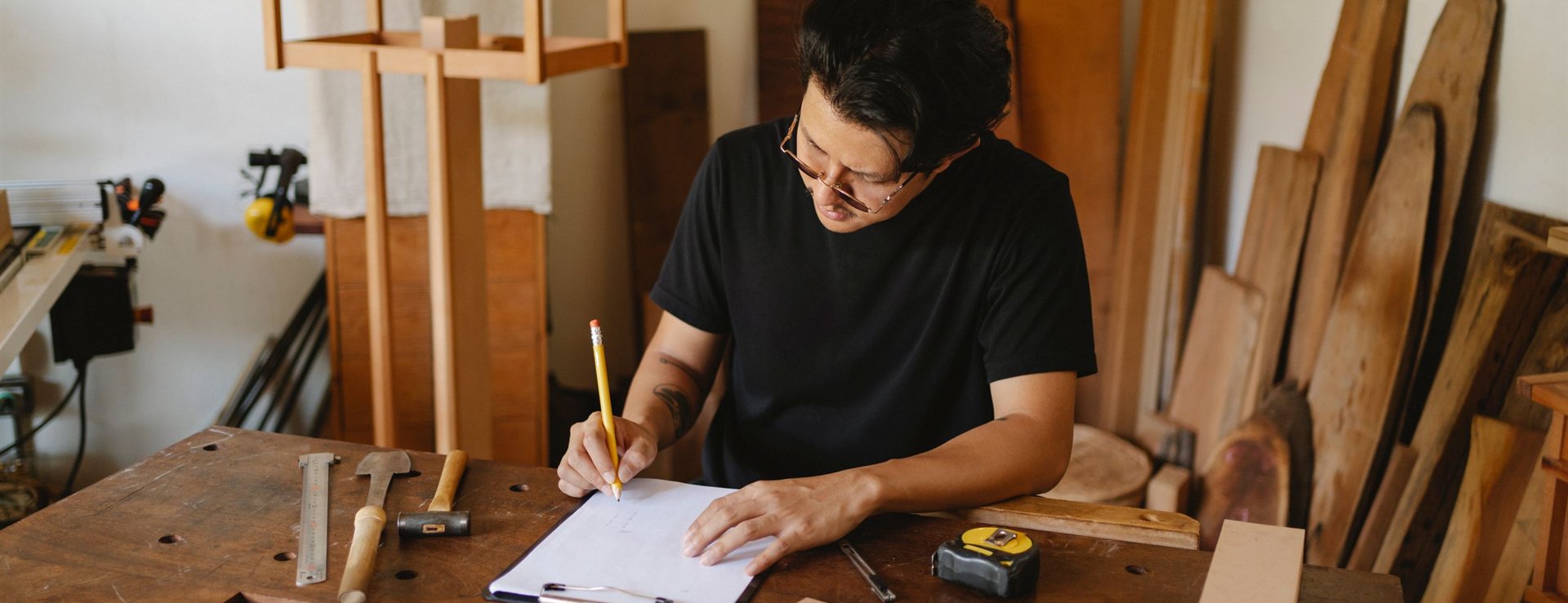 Craftsman sketching a new product design at a workshop bench with tools and timber